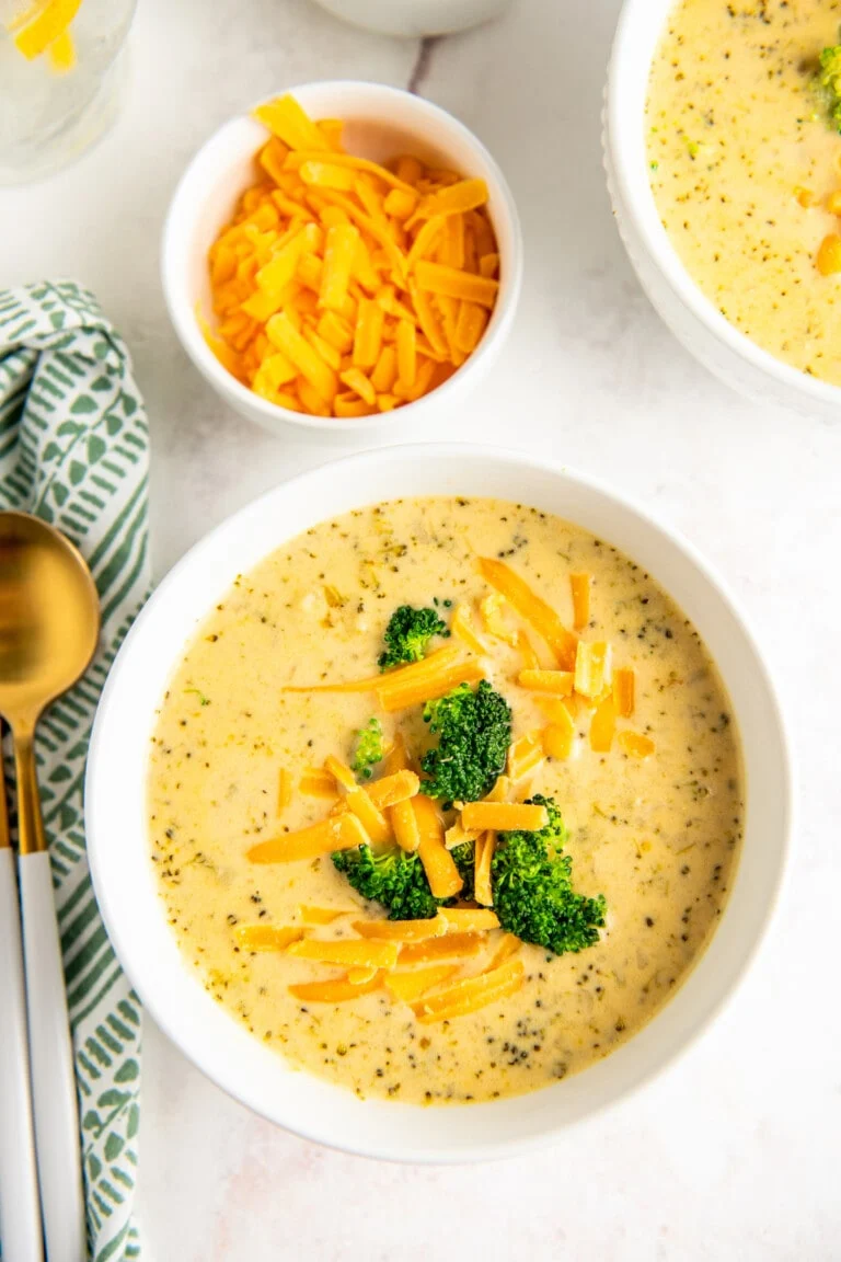 "A close-up view of creamy Crockpot Broccoli Cheese Soup in a white bowl, garnished with extra shredded cheddar cheese and a sprinkle of black pepper." "A steaming bowl of homemade slow cooker broccoli cheddar soup loaded with tender broccoli florets and shredded carrots."